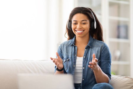 Foto de Mujer afroamericana sentada en un sofá con auriculares puestos, escuchando música o un podcast. Ella aparece relajada y enfocada en el sonido que viene de sus auriculares. - Imagen libre de derechos