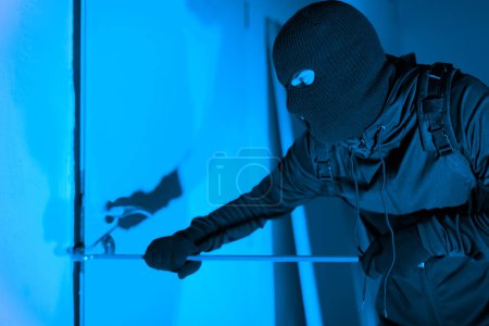 A caught-in-action shot of a thief cautiously opening a glass door while exiting, denoting the silent danger of burglary at an apartment at night