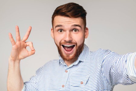 Happy millennial guy showing OK sign on camera and making selfie, panorama