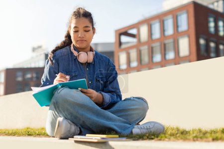 A young girl is seated on the ground, engrossed in a book and wearing headphones. She appears focused and relaxed as she enjoys her reading and music.