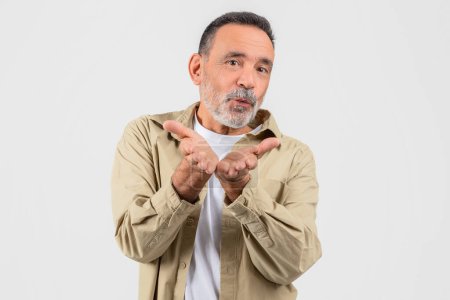 A charismatic elderly man blows a kiss with a hand gesture, showing affection and warmheartedness, isolated on a white background
