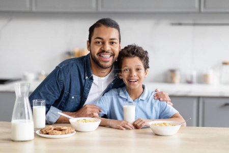 Téléchargez les photos : Le lien intime entre un père afro-américain et son fils alors qu'ils prennent leur petit déjeuner ensemble dans une cuisine évoque l'esprit des liens familiaux - en image libre de droit