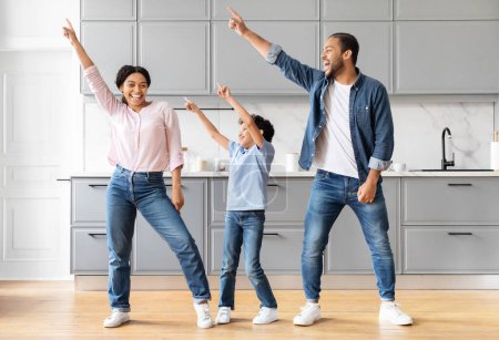 Foto de Graciosa familia afroamericana positiva bailando en la cocina gris moderna, feliz padre negro madre e hijo disfrutando del tiempo juntos en casa - Imagen libre de derechos