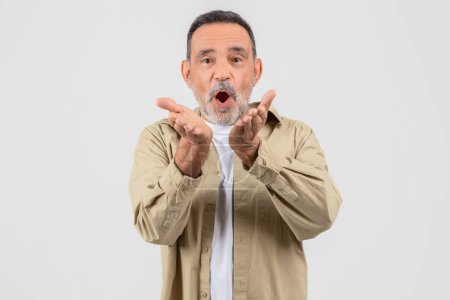Ein älterer Mann im Hemd ist zu sehen, wie er mit den Händen eine Geste macht. Er scheint ausdrucksstarke Körpersprache zu verwenden, um eine Botschaft zu kommunizieren oder einen Punkt hervorzuheben.