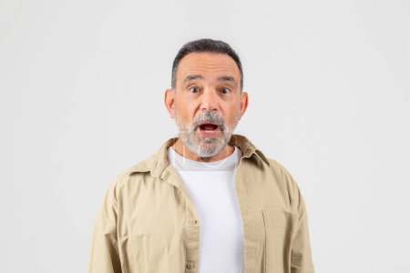 Photo for A senior man with a look of surprise on his face, eyebrows raised, mouth slightly agape. His eyes are wide, indicating shock or astonishment. He appears taken aback by something unexpected. - Royalty Free Image