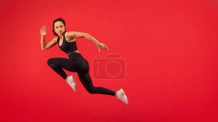 Foto de Una mujer que lleva un top negro y polainas negras es capturada en medio del salto en el aire. Sus brazos están extendidos y sus piernas dobladas, mostrando su atletismo y agilidad mientras desafía la gravedad. - Imagen libre de derechos
