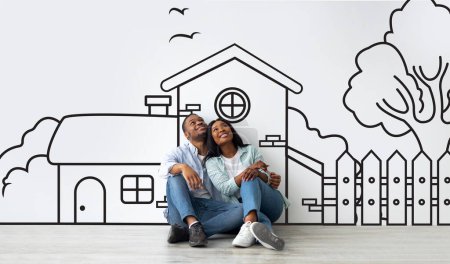 Foto de Pareja afroamericana amorosa planeando su casa de ensueño contra un boceto de casa dibujado a mano sobre fondo blanco de la pared. Concepto hipotecario - Imagen libre de derechos
