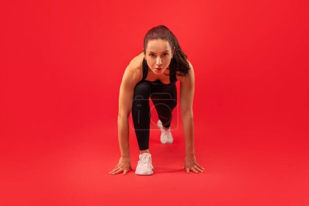 Téléchargez les photos : Une femme vêtue de vêtements noirs exécute une position debout, en équilibre sur ses mains avec les jambes tendues vers le haut, arrière-plan studio rouge - en image libre de droit