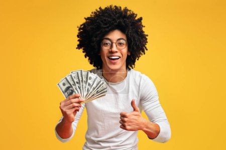 Photo for Saving money concept. Happy african-american guy holding bunch of money and showing thumb up gesture, orange background - Royalty Free Image