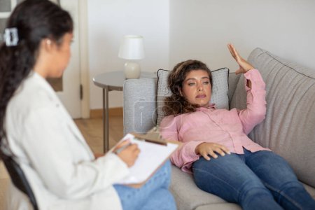 Emotionale junge Frau mit Angstzuständen, Liegen auf dem Sofa in der Klinik, Austausch ihrer Gedanken, therapeutische Sitzung mit Psychologen