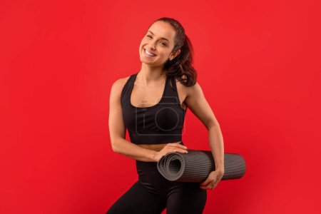 Photo for A woman standing while holding a yoga mat and smiling brightly. She appears joyful and ready for her yoga practice. - Royalty Free Image