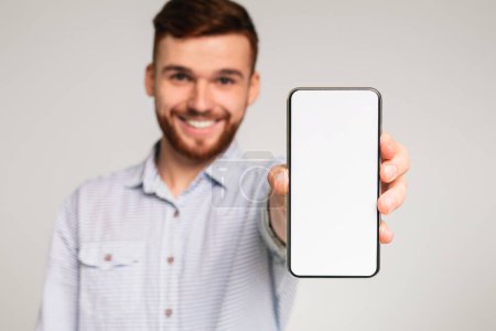 Téléchargez les photos : Jeune homme montrant son téléphone avec un espace vide sur la caméra et souriant, panorama - en image libre de droit
