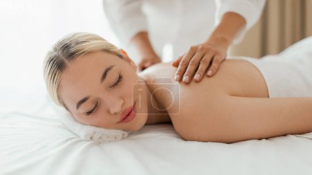 Téléchargez les photos : Une femme couchée face contre terre sur une table de massage dans un spa, recevant un massage du dos d'un massothérapeute, panorama - en image libre de droit