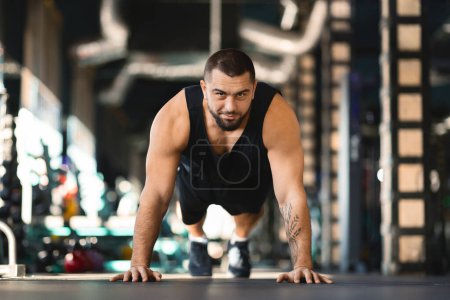 Un hombre está realizando flexiones en un gimnasio, demostrando fuerza y resistencia. Él está enfocado y determinado, con los músculos comprometidos y el cuerpo en línea recta