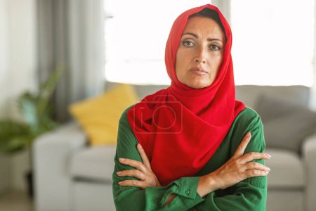 A woman is depicted wearing a hijab that is predominantly red with green accents. She appears to be looking directly at the camera, with a serene expression on her face.