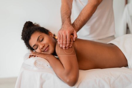 A spa scene with a black lady experiencing a peaceful back rub, highlighted by the therapists hands and a comforting spa ambiance