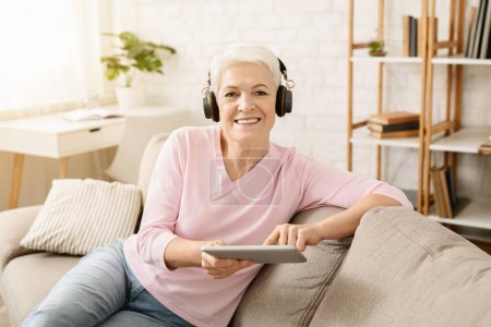 Téléchargez les photos : Femme âgée profiter de la musique et regarder des vidéos sur tablette PC dans les écouteurs, espace libre - en image libre de droit