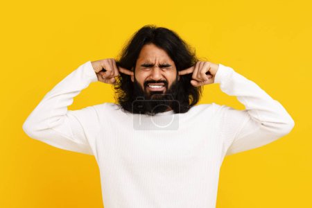 Foto de Hombre indio con el pelo largo y una barba se muestra sosteniendo sus manos en las orejas, lo que indica un gesto de bloquear el ruido o proteger sus oídos de los sonidos fuertes - Imagen libre de derechos