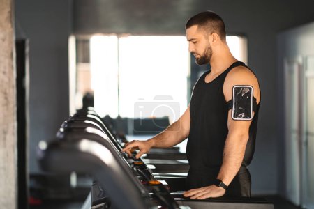 Ein Mann mit schwarzem Tanktop läuft energisch auf einem Laufband in einem Fitnessstudio. Er ist fokussiert und entschlossen, wobei seine Hände die Seitenschienen nach Stabilität greifen, während er an seine Grenzen stößt..