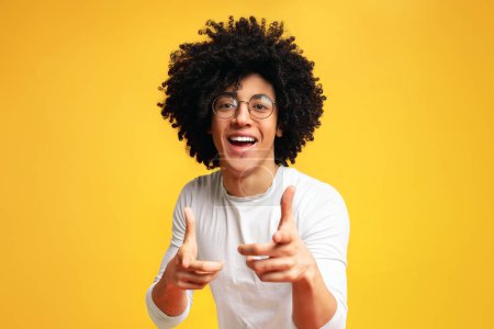 Hey du. Fröhlicher schwarzer Mann in Brille zeigt glücklich in die Kamera, wählt den Wettbewerb, orangefarbener Studiohintergrund