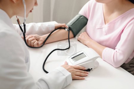 A doctor is using a stethoscope to measure a patients blood pressure in a medical setting. The doctor is focused on listening to the patients heartbeat and recording the readings on a medical chart.