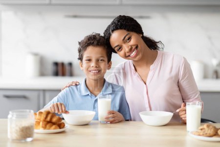 Téléchargez les photos : Une joyeuse mère afro-américaine et son fils sont montrés souriants à la table de la cuisine, affichant un moment de bonheur et de convivialité - en image libre de droit