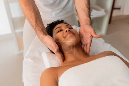 Téléchargez les photos : Les mains professionnelles se concentrent sur le massage du cou d'une femme noire, soulignant l'importance de l'autosoin dans un spa - en image libre de droit