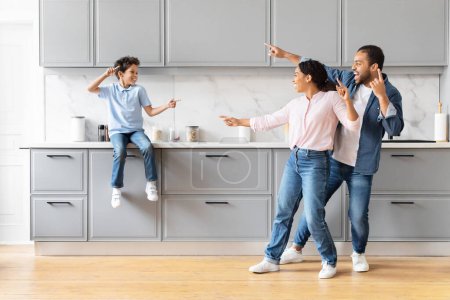 Photo for Happy African American family father mother and preteen son having fun together in kitchen, imitating fight and laughing - Royalty Free Image