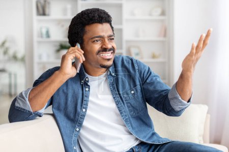 Photo for Cheerful african american guy enjoying a phone call at home, representing lighthearted communication - Royalty Free Image