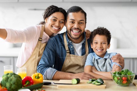 Foto de Alegre familia afroamericana padres con niño tomando una selfie mientras cocinan juntos en la cocina - Imagen libre de derechos