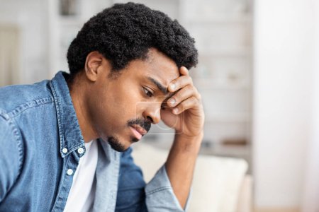 With visible distress or shame, a black guy covers his face with his hands while at home, suggesting despair, privacy concerns or a moment of intense emotions