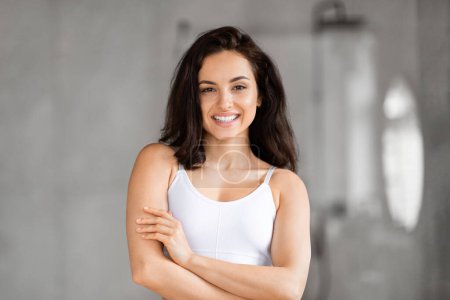 Smiling millennial pretty brunette lady wearing top proudly showing her healthy skin in a bright bathroom setting