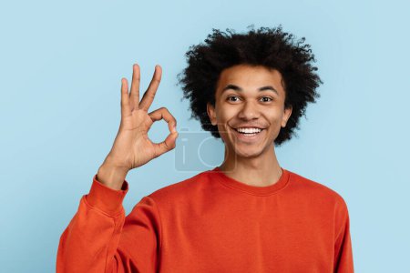 Téléchargez les photos : Afro-américain confiant montrant le geste de la main OK, signalant l'approbation ou la satisfaction, isolé sur un fond bleu, reflétant la positivité et l'accord - en image libre de droit