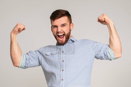 Photo for Young muscular man showing his power in biceps on camera at beige background, panorama, copy space - Royalty Free Image