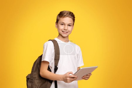 Foto de Educación y tecnologías modernas. Colegial con mochila usando tableta y sonriendo sobre fondo naranja, espacio vacío - Imagen libre de derechos