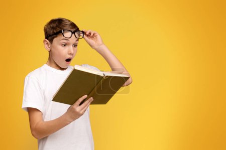 Téléchargez les photos : Un jeune garçon portant des lunettes est absorbé par la lecture d'un livre. - en image libre de droit