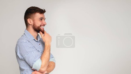 Jeune homme souriant réfléchissant et regardant loin sur l'espace libre sur fond de studio, panorama, espace libre
