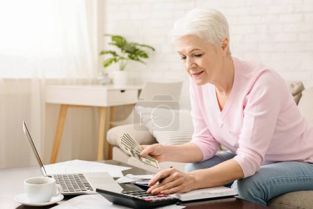 Photo for Senior woman with calculator and bills counting dollar money at home, free space - Royalty Free Image