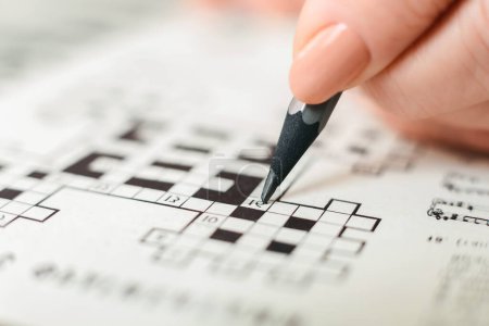 Photo for A person is seen actively engaged in a crossword puzzle, holding a pencil and carefully filling in the boxes with letters. The crossword grid is visible, showing a mix of empty and filled squares. - Royalty Free Image