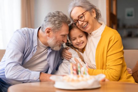 Foto de Hombre y mujer mayores están sentados al lado de una niña frente a un pastel de cumpleaños. Parecen estar celebrando una ocasión especial, posiblemente un cumpleaños, con el pastel como la pieza central - Imagen libre de derechos