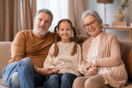 Photo for A heartwarming scene captures a young girl seated between her grandparents, sharing a moment of joy at home interior - Royalty Free Image