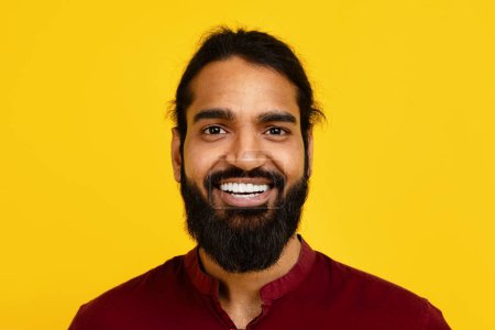 Photo for Millennial Indian man with a beard is smiling directly at the camera, showing a warm and friendly expression. His beard is well-groomed, and his eyes are crinkled at the edges from smiling. - Royalty Free Image