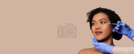 Photo for A brazilian woman is seated while a healthcare professional, wearing sterile blue gloves, administers a cosmetic injection to her facial area, panorama with copy space - Royalty Free Image
