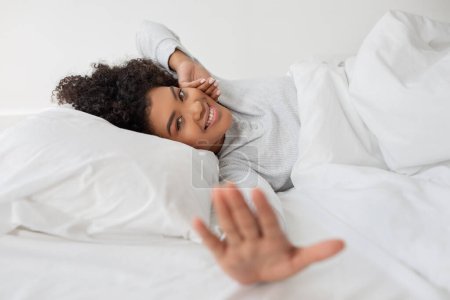 Téléchargez les photos : Une femme est vue allongée au lit avec une couverture blanche couvrant son corps, s'étirant. Elle semble se reposer confortablement dans un cadre confortable. - en image libre de droit