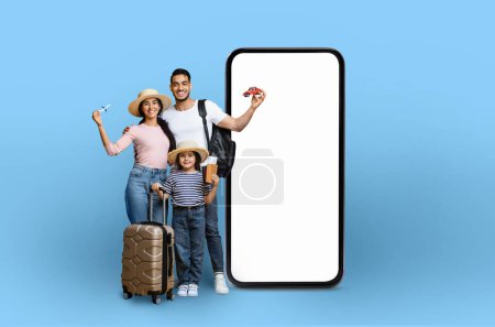 Foto de Una familia con equipo de viaje y un coche de juguete junto a un teléfono inteligente maqueta, que ilustra la tecnología de planificación de viajes, aislado sobre un fondo azul - Imagen libre de derechos