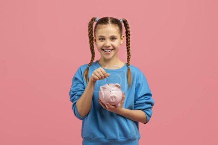 A smiling young girl with braided hair is about to insert a coin into a pink piggy bank against a bright pink background