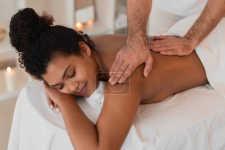 A therapist meticulously works on an african american ladys shoulder at a spa, concentrating on relieving tension in a people-focused image