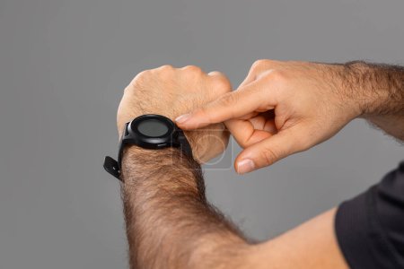 A man in casual attire is checking the time on a wristwatch he is wearing on his left wrist. The watch face is visible, indicating his focus on time management, cropped