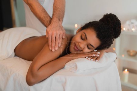 Foto de Una vista íntima de una dama negra recibiendo un relajante masaje de espalda en un acogedor spa, con un enfoque en las manos y la comodidad - Imagen libre de derechos