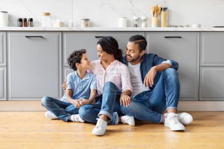 Photo for Loving black family sharing a moment of connection while seated on the kitchen floor, evoking warmth and affection - Royalty Free Image